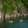 Tourists kayaking along the lush limestone cliffs of Ha Long Bay, enjoying the natural beauty and adventure offered by Peony Cruise
